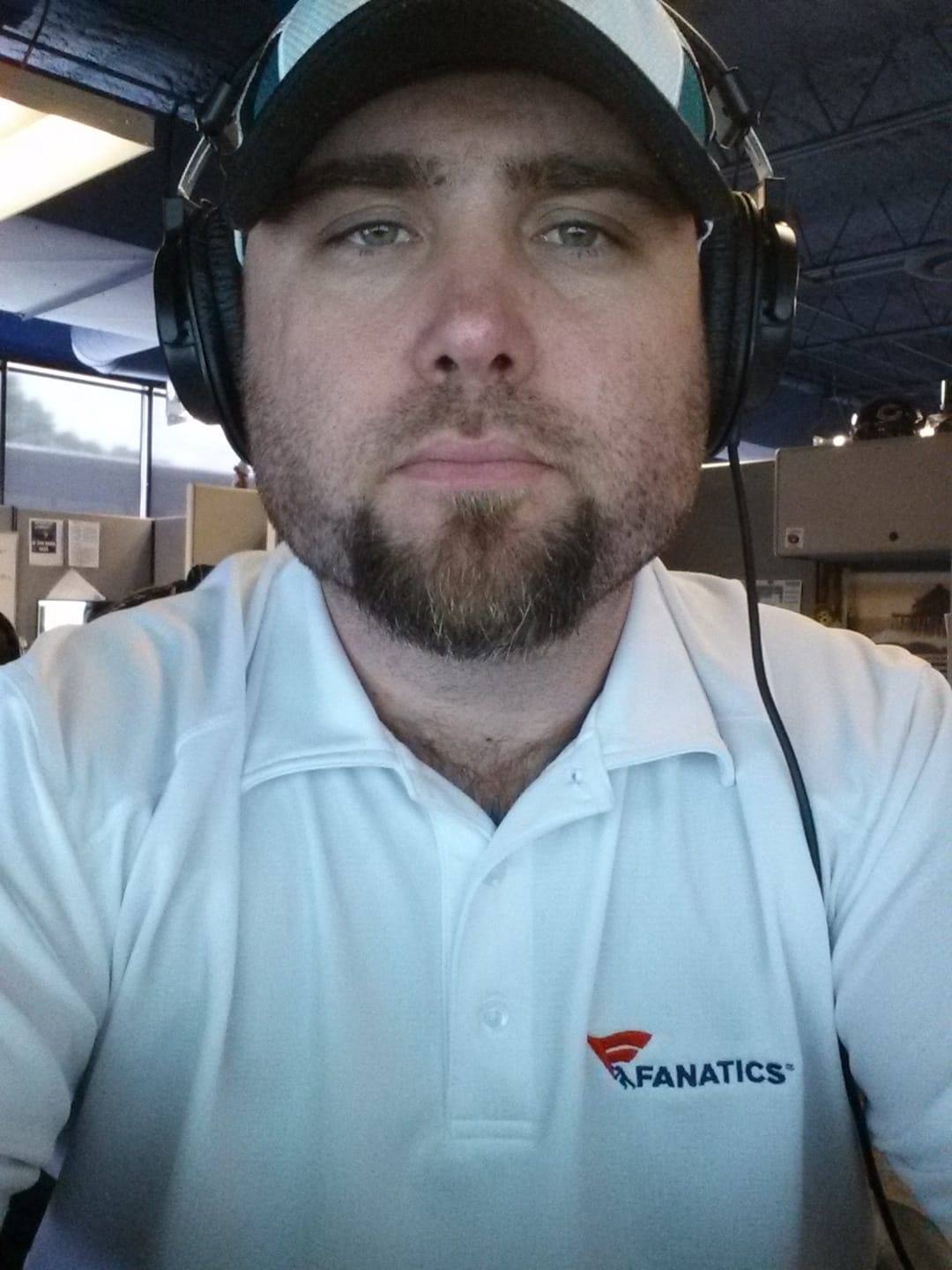 A selfie of Marshall Malone in a white Fanatics branded polo, with headphones on at work in the SEO department.